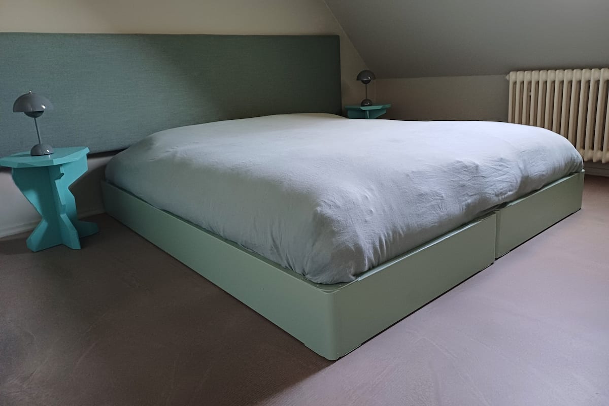 Ein Schlafzimmer mit einem Bett, einem Nachttisch, einer Lampe und einer Heizung.