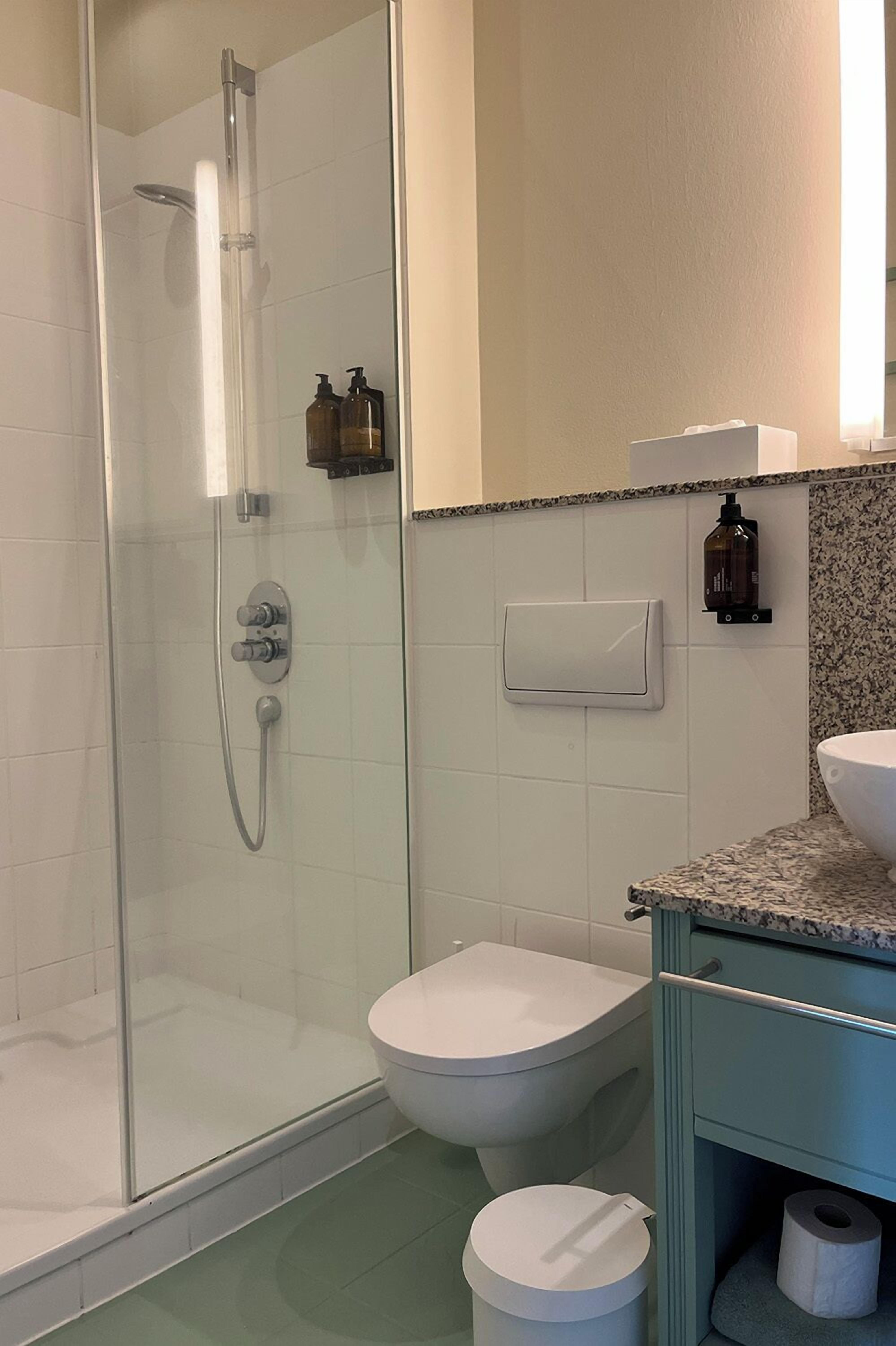 Un baño con ducha de vidrio, inodoro y lavamanos con encimera de granito.