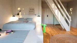 Een slaapkamer met een bed, nachtkastjes, een groene prullenbak, een trap en een deur.