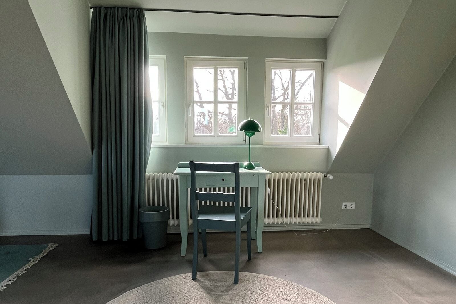 Una habitación con escritorio, silla, radiador y ventana con cortinas.