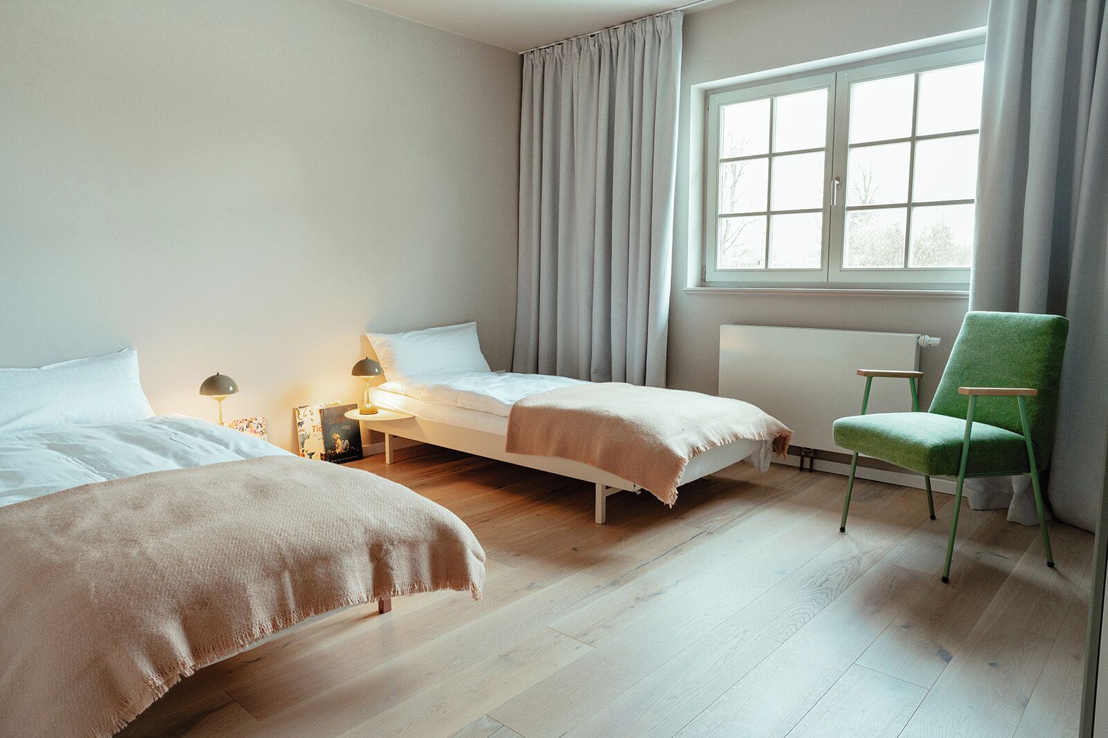 A hotel room with two beds, a chair, a window, and a radiator.