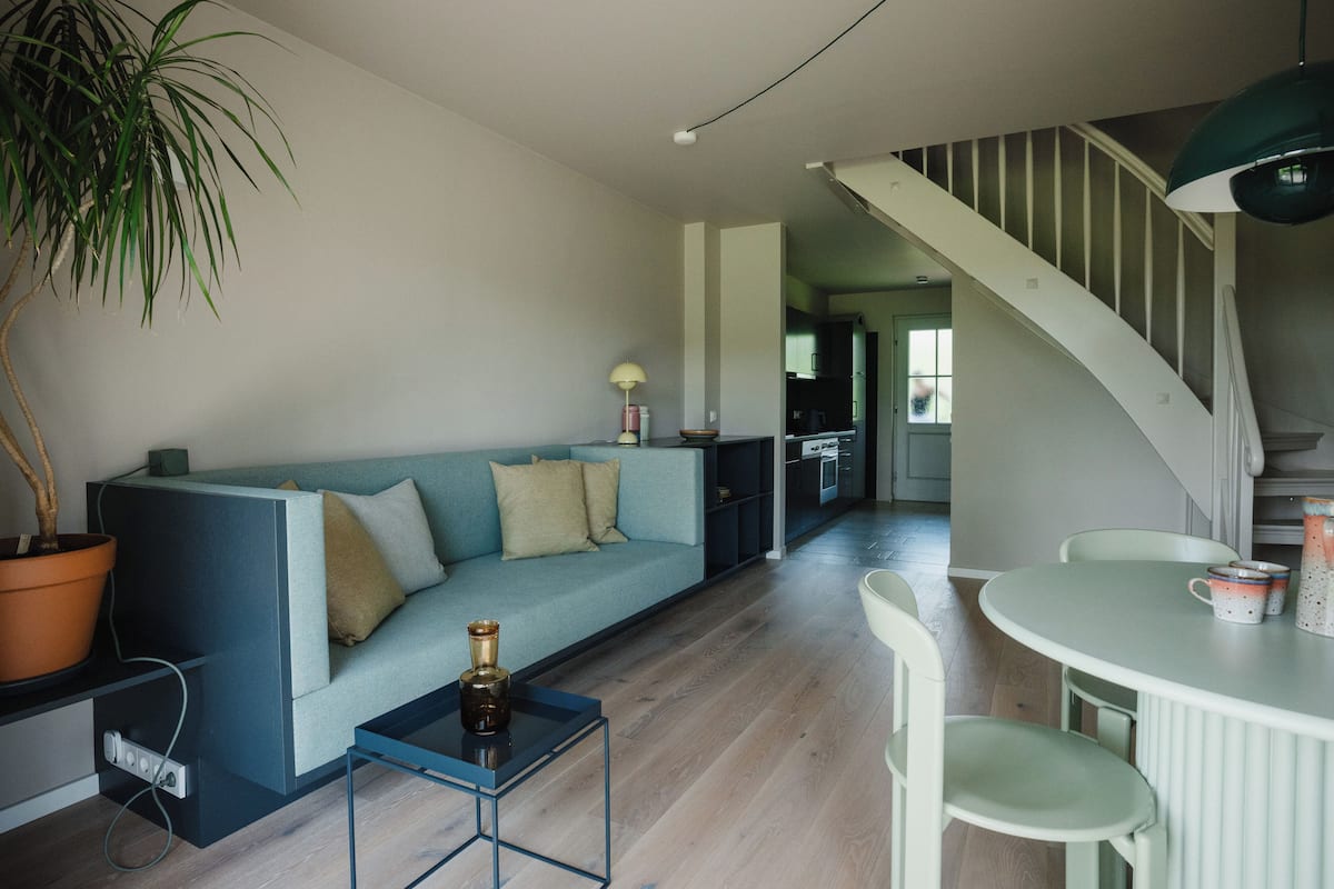 Ein modernes Wohnzimmer mit einem blauen Sofa, einem kleinen Tisch, einer Topfpflanze und einer Treppe, die in einen anderen Bereich führt.