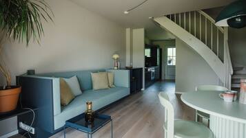 A modern living room with a blue sofa, a small table, a potted plant, and a staircase leading to another area.