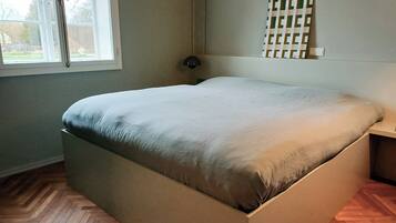 Een kamer met een bed, een raam, een wandlamp en een visgraatparketvloer.