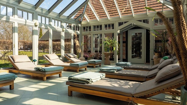 Een veranda met meerdere lounge fauteuils en een glazen dak.