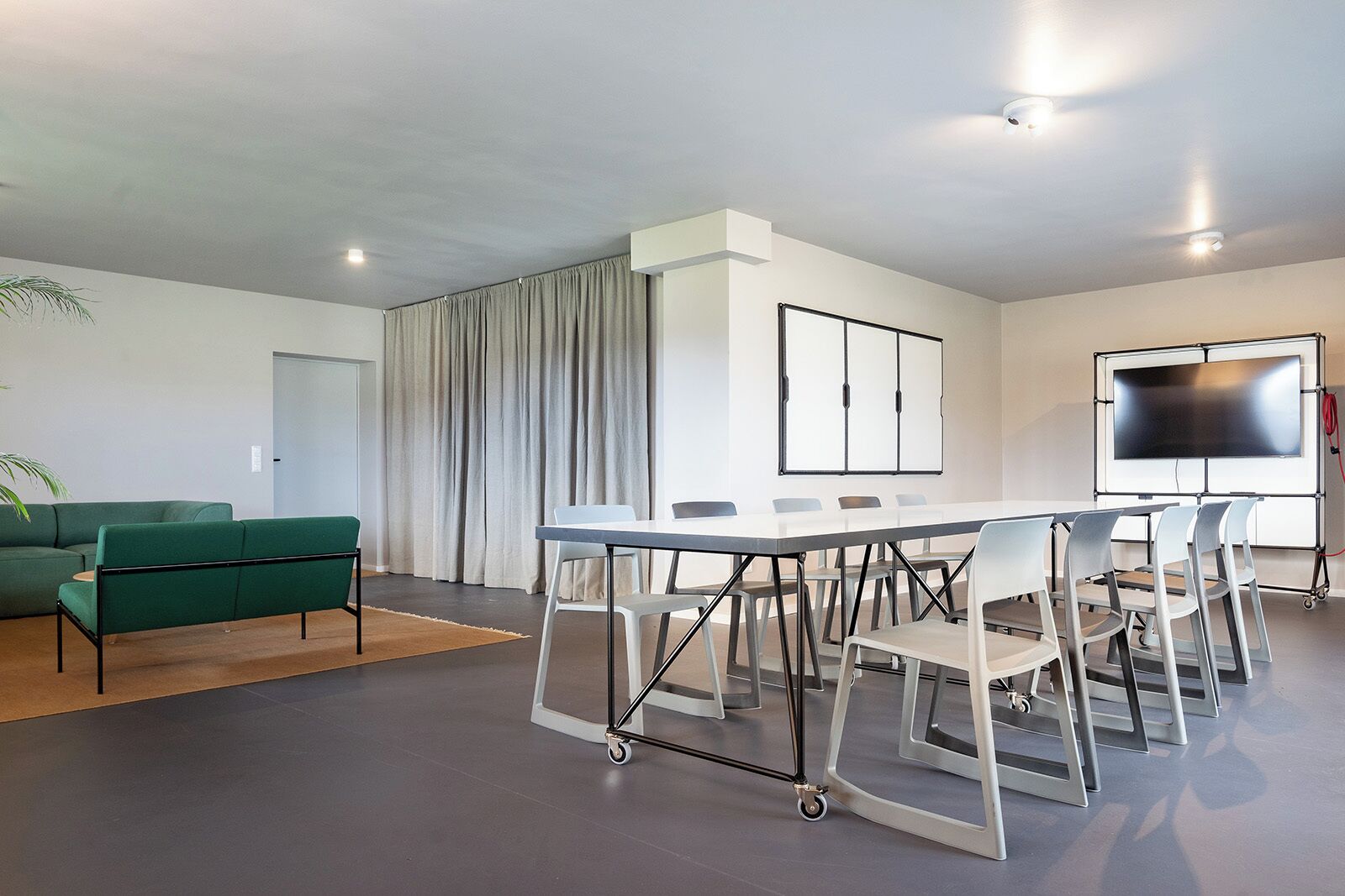 Een moderne vergaderruimte met een witte tafel, grijze stoelen, een groene bank en een groot scherm.