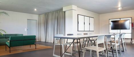 A modern meeting room with a white table, grey chairs, a green sofa, and a large screen.