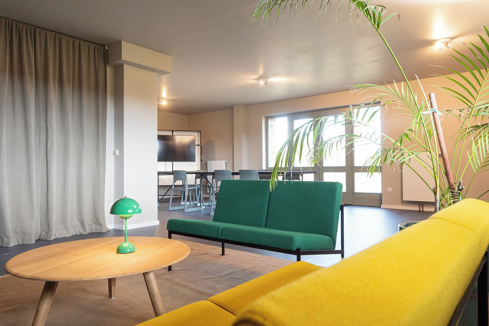 A modern living room with a green sofa, yellow armchair, and a round wooden table with a green lamp.