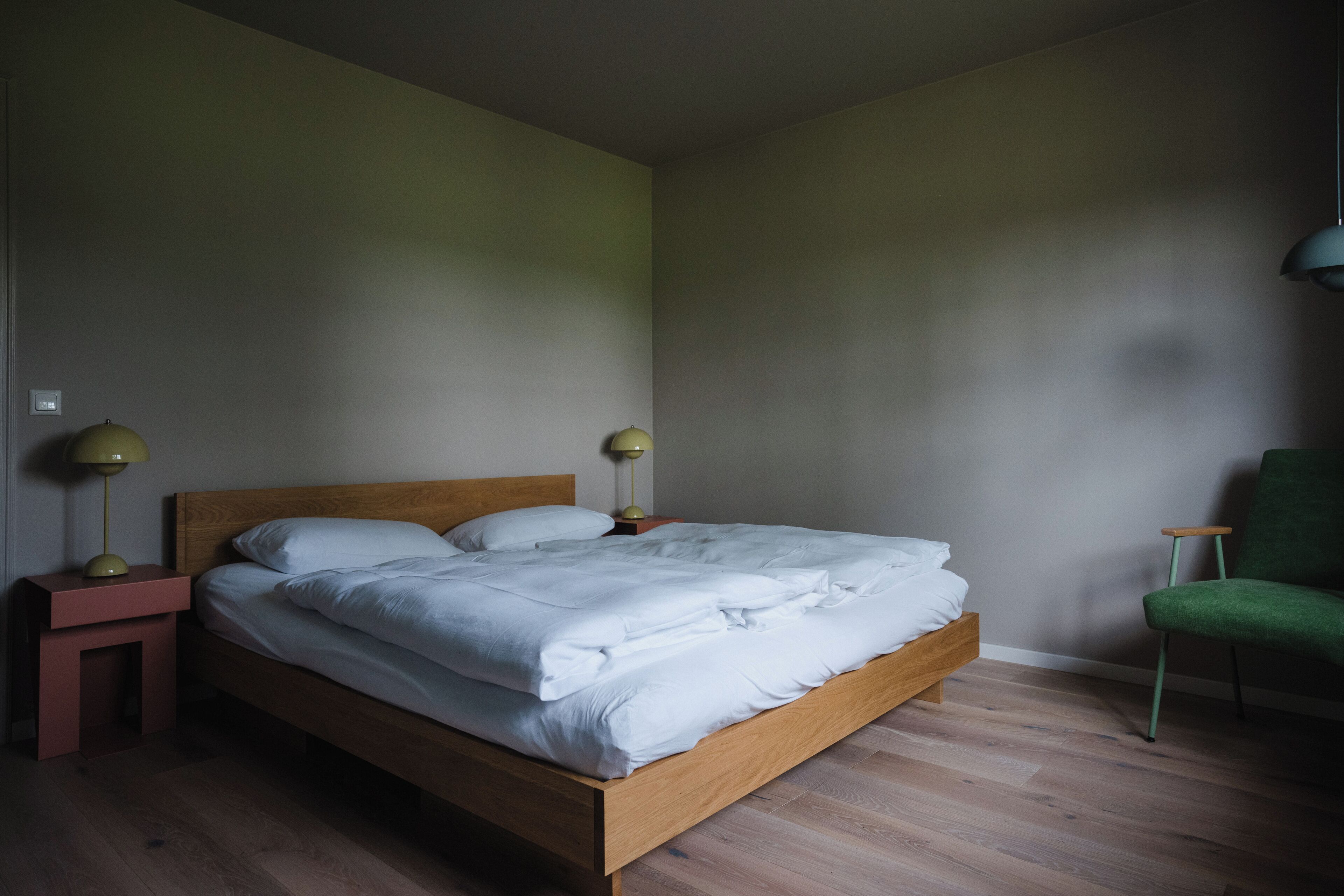 A bedroom with a wooden bed, two bedside tables with lamps, a green chair, and a wooden floor.