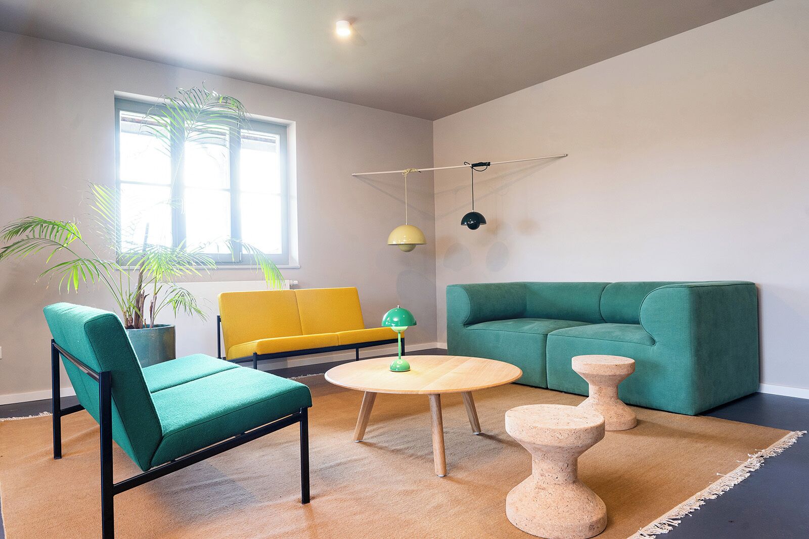 A living room with a green sofa, a yellow armchair, a round wooden table, and a potted plant.