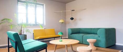 Una sala de estar con un sofá verde, un sillón amarillo, una mesa redonda de madera y una planta en maceta.