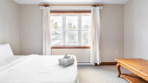 Ein Hotelzimmer mit einem Bett, einer Holzbank und einem großen Fenster mit Vorhängen.