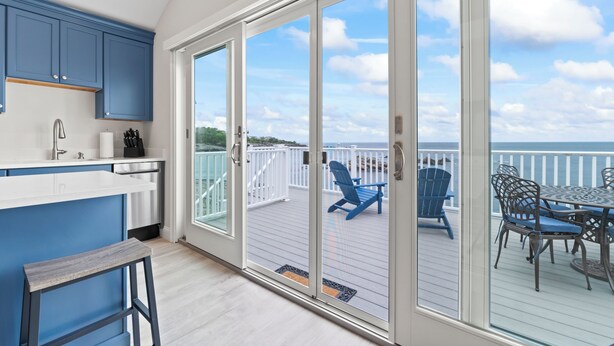 A modern kitchen with blue cabinets, a white countertop, and a sliding glass door leading to an outdoor deck with a table and chairs.
