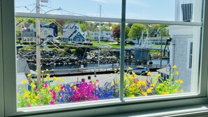 A view through a window with a flower box in the foreground, a bridge, and houses in the background.
