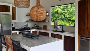 A modern kitchen with a large island, wooden cabinets, and a large window with a view of greenery.