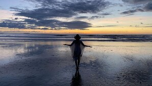 A person walking on a beach at sunset with a cloudy sky.