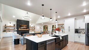 A modern kitchen with a large island, black cabinetry, white countertops, and pendant lighting.