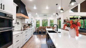 A modern kitchen with white cabinetry, a black range hood, and a built-in oven.