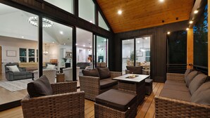A spacious living area with wicker furniture, large windows, and a wooden ceiling.