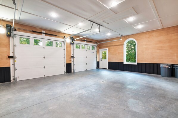A spacious garage with three white garage doors, a concrete floor, and wooden walls.