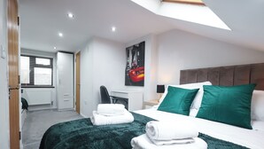 Una habitación de hotel moderna con una cama, almohadillas verdes, un escritorio y un cuadro de un paisaje urbano.