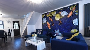Una sala de estar moderna con un sofá azul oscuro, una mesa de centro de vidrio y un mural abstracto lleno de color.