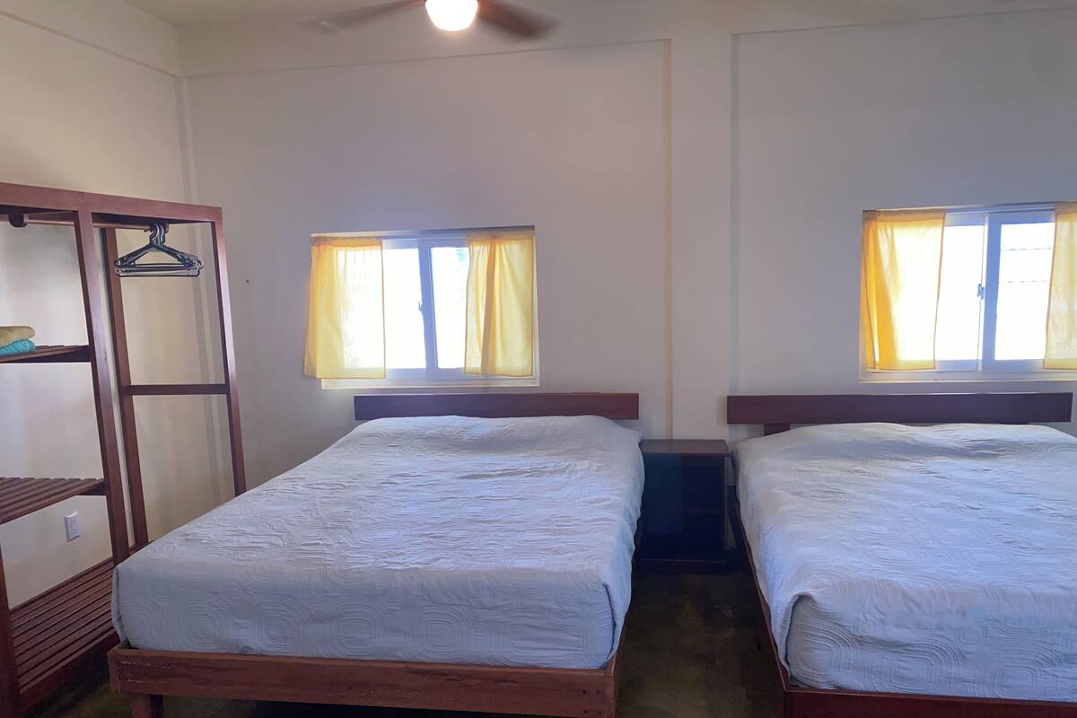Een kamer met twee houten bedden, een houten kledingkast en een plafondventilator.