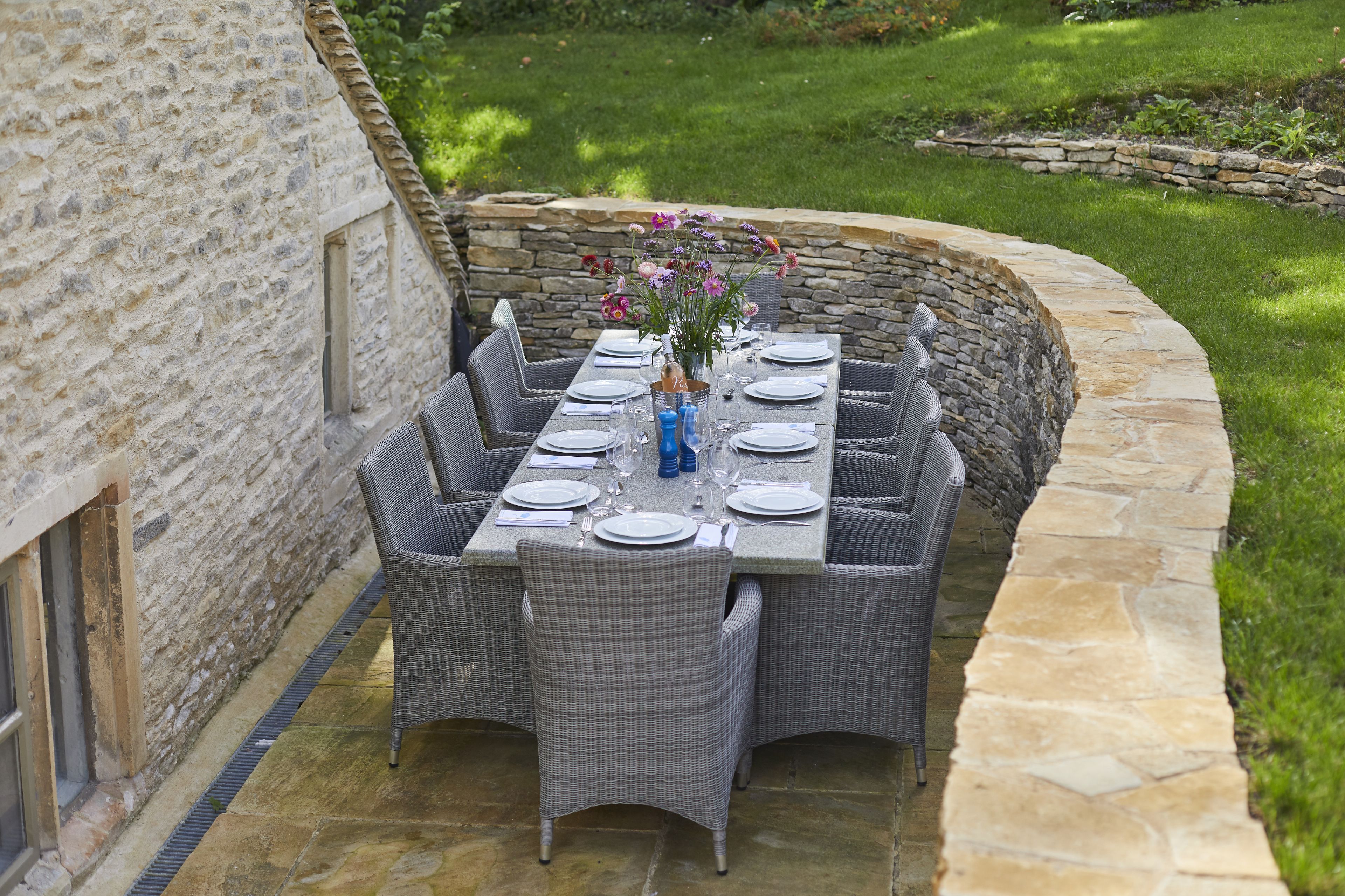 An outdoor dining area with a stone wall, wicker furniture, and a table set for six.