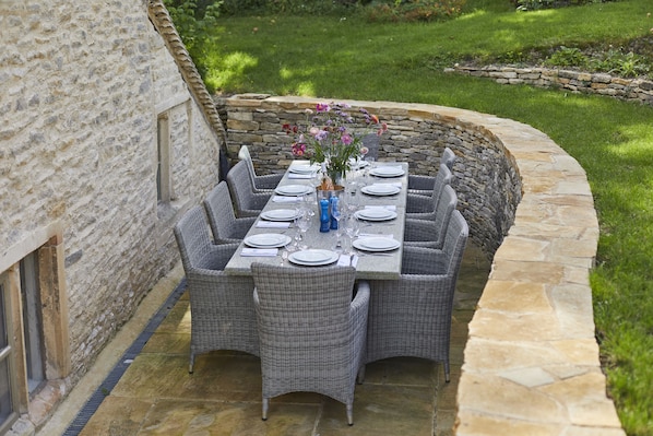 An outdoor dining area with a stone wall, wicker furniture, and a table set for six.