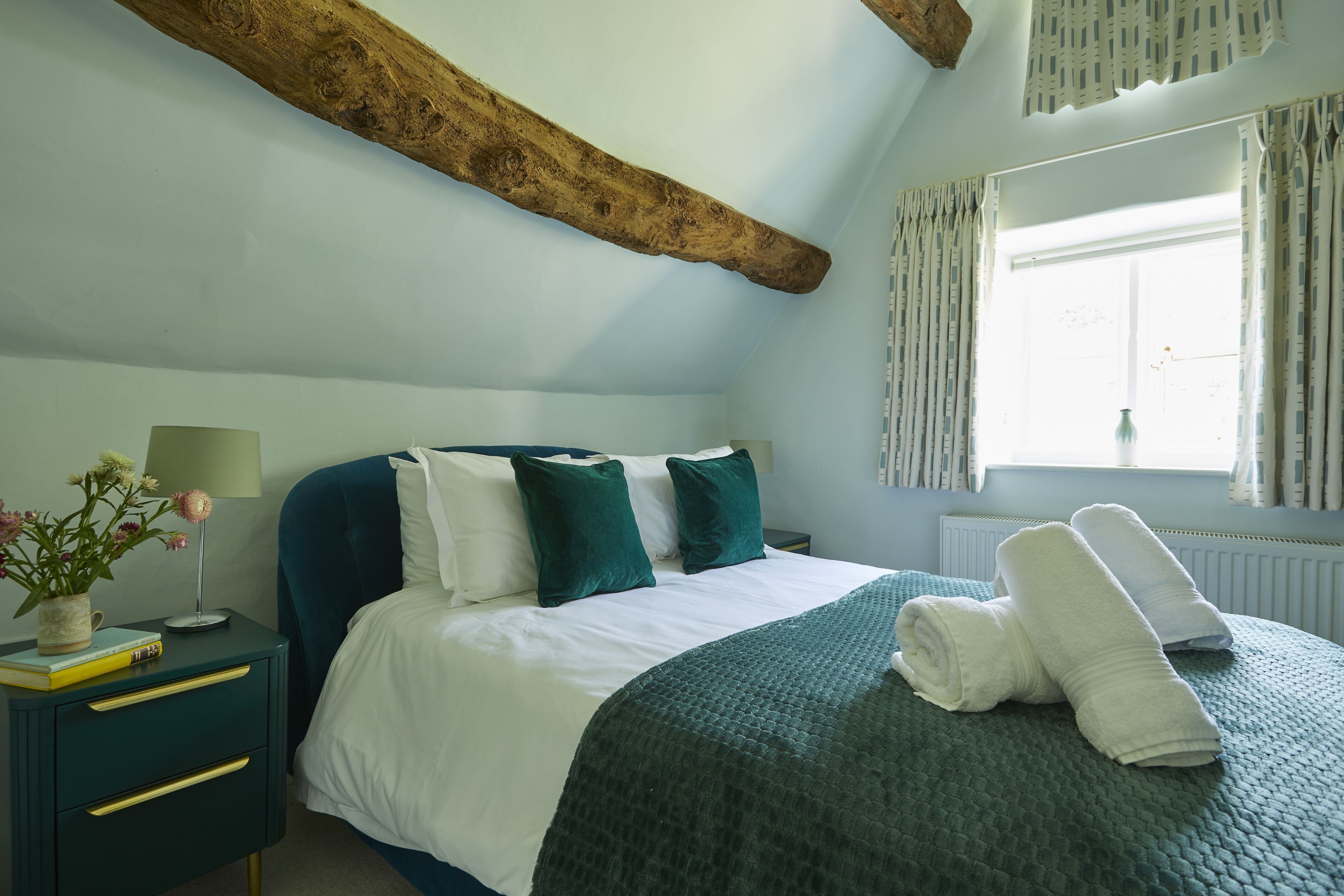 A bedroom with a bed, pillows, a nightstand, a lamp, and a window with curtains.