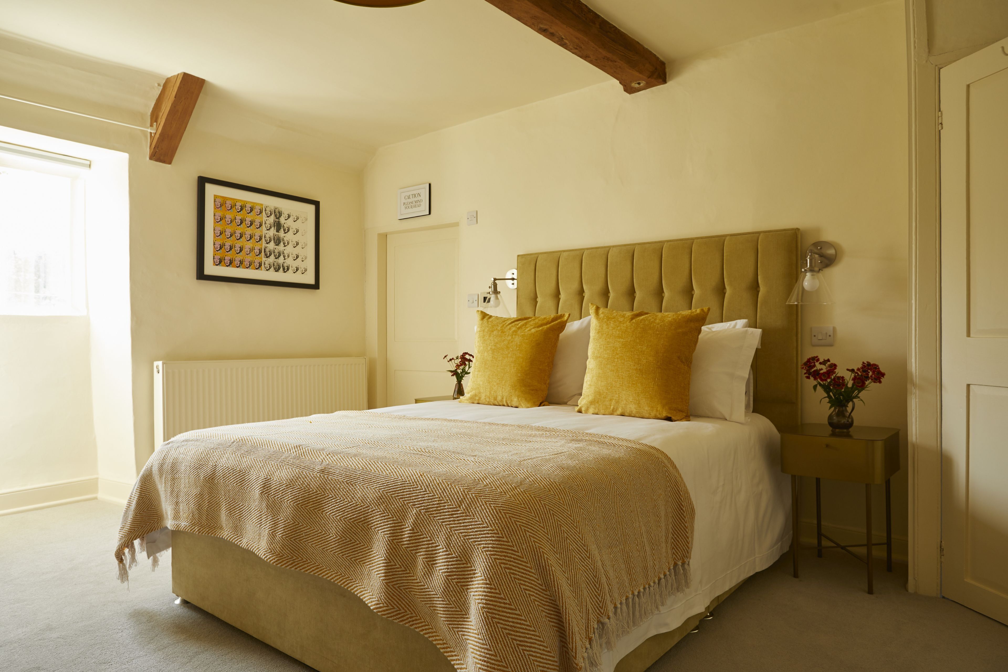Ein Schlafzimmer mit einem großen Bett, einem Kopfteil, einem Nachttisch mit Lampe und einem gerahmten Bild an der Wand.