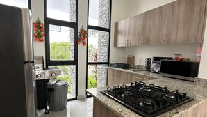 Een moderne keuken met een centraal kookeiland, roestvrijstalen apparatuur en grote ramen met uitzicht op groen.