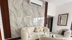 Een moderne woonkamer met een marmeren wand, een beige bank, een bijpassende fauteuil en een klein bijzettafeltje.