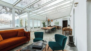 A spacious living area with a large sofa, teal armchairs, and a coffee table. A dining area with a wooden table and chairs is visible in the background. - Villa La Felice (pianello del lario)