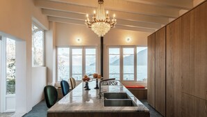 A modern kitchen with a marble countertop, wooden cabinets, and a large window overlooking a body of water. - Villa La Felice (pianello del lario)