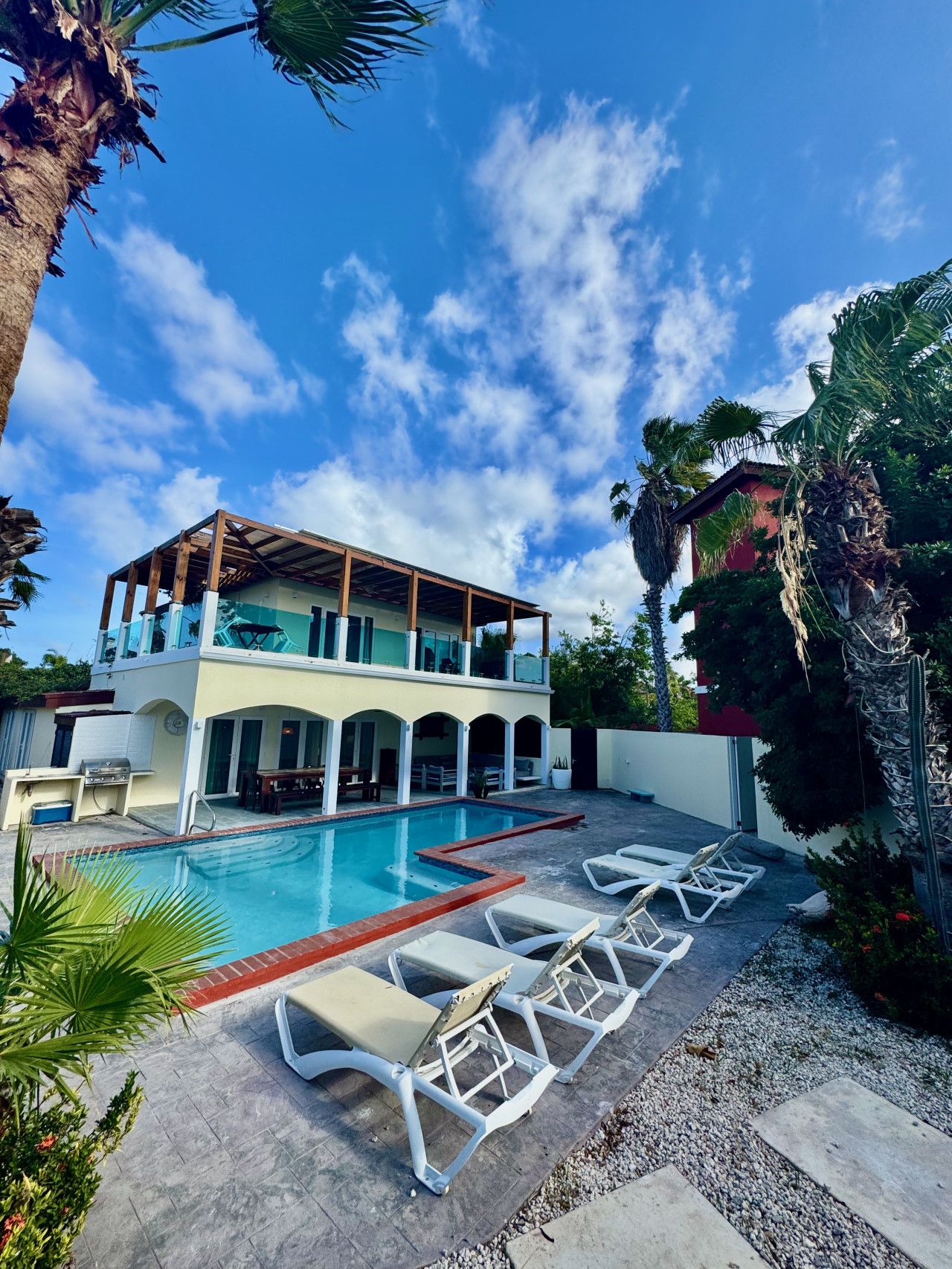 A two-story house with a swimming pool, lounge chairs, and a barbecue area.