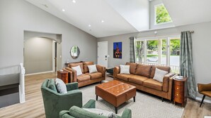 Een ruime woonkamer met een hoge plafond, twee leren banken, een groene fauteuil en een kamerkleed met patroon.