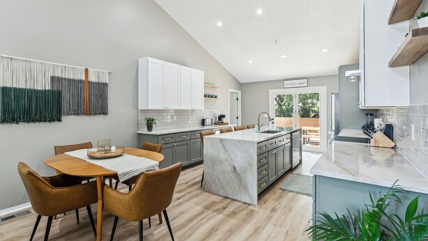 Een moderne keuken met een centraal eiland, grijze kastjes en een eethoek met een houten tafel en stoelen.
