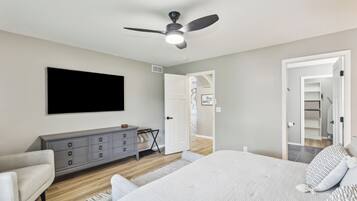 Quarto com cama, penteadeira, ventoinha no teto e TV fixada na parede.