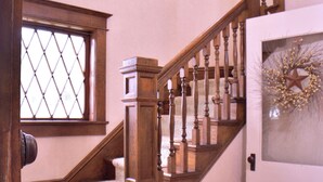 A wooden staircase with a carpeted landing, a door with a decorative wreath, and a window with a diamond pattern.