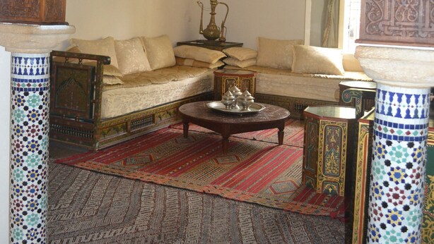 A traditional Moroccan interior with a sofa, patterned rugs, and ornate wooden carvings. - Accommodation decorated with Moroccan craftsmanship (Rabat)