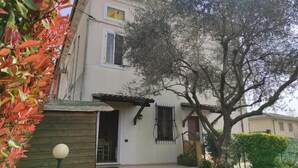 A two-story house with a garden, a wooden fence, and a tree in front.