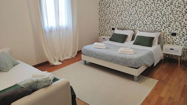 A bedroom with a bed, a bedside table, a nightstand, a window with curtains, and a wall with a leaf pattern.