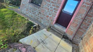 A stone building with two windows, a door, and a paved entrance area. - Luichart Lodge (Garve)