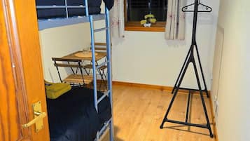 Una habitación pequeña y funcional con literas, una ventana con cortinas y un radiador.