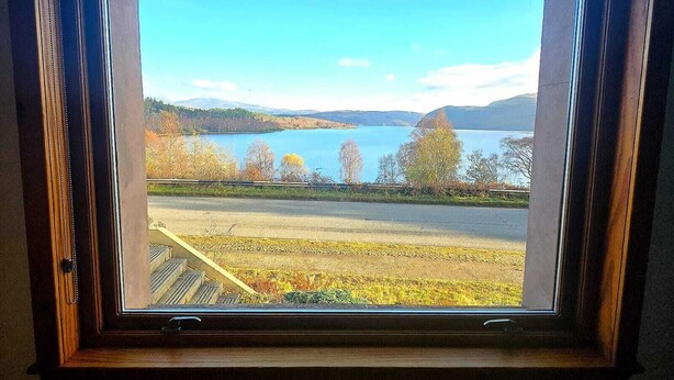 A window with a view of a lake, trees, and a distant mountain range. - Luichart Lodge (Garve)