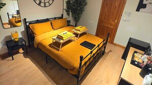 A bedroom with a bed, a bedside table, a mirror, a clock, a door, and a small desk with a chair. - Luichart Lodge (Garve)