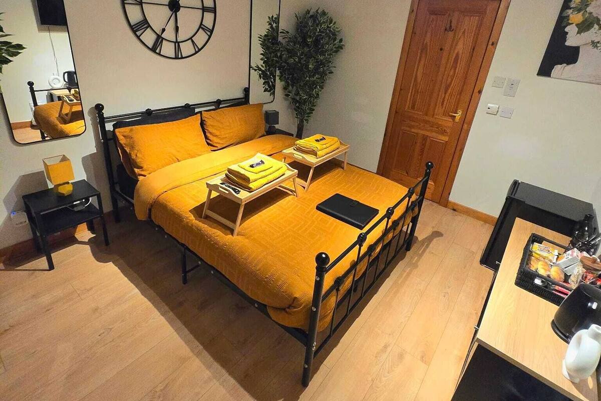 Une chambre à coucher comprenant un lit, une table de chevet, un miroir, une horloge, une porte et un petit bureau avec une chaise.