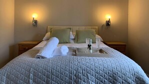 Ein ordentlich bezogenes Bett mit einer gesteppten Decke, zwei Kissen und einem Tablett mit Gläsern und einer Flasche.