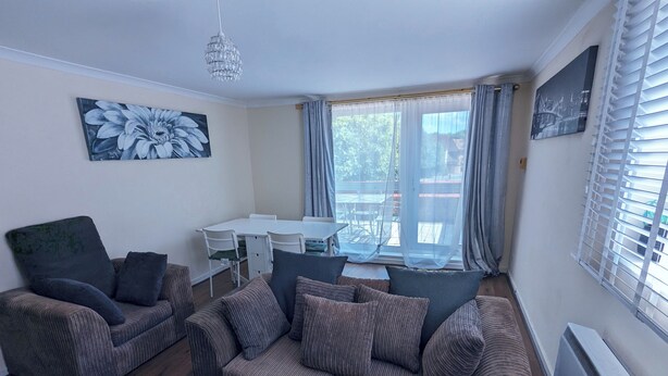 A living room with a sofa set, a dining table, and chairs. There is a large window with curtains, a chandelier, and a painting on the wall. - A&A Apartment Basildon with free parking  (Basildon)